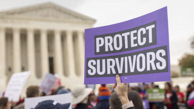 In the image foreground, a person's hand and wrist is visible with pink silicon watch band. They hold a 
