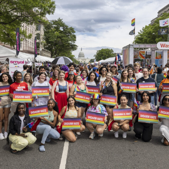 A group of about 20 students pose in two rows, many of them holding signs that say 