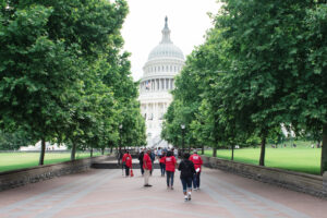 Moms Demand Action volunteers in red t-shirts walk along a tree-lined path toward the U.S. Capitol Building in Washington, D.C.