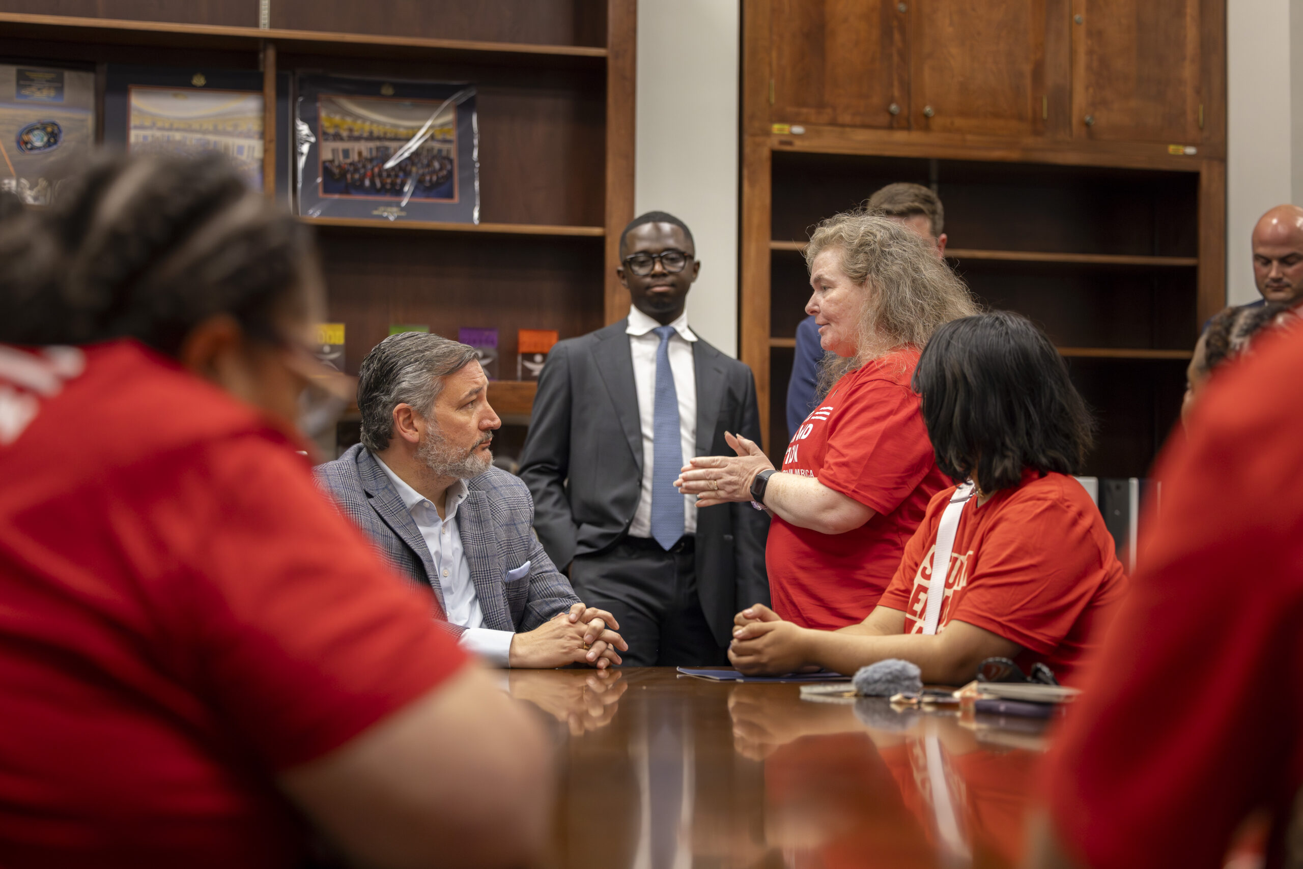 A side-profile picture of Ted Cruz and a Moms Demand Action volunteer. Cruz is looking up at the volunteer, who has her hands pressed together and pointed at him. 