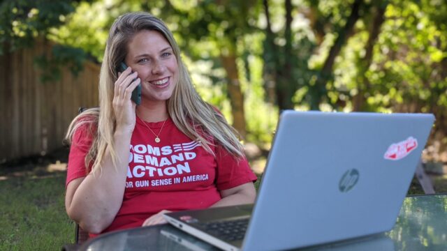 A woman wearing a Moms Demand Action shirt sits outside while phonebanking