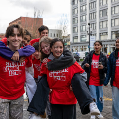 Students Demand Action volunteers pose for a group photo. Two students are being piggy-backed by two others. All are wearing red Students Demand Action t-shirts.