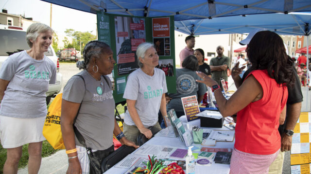 Three Be SMART volunteers talk about secure gun storage while tabling at a community event.
