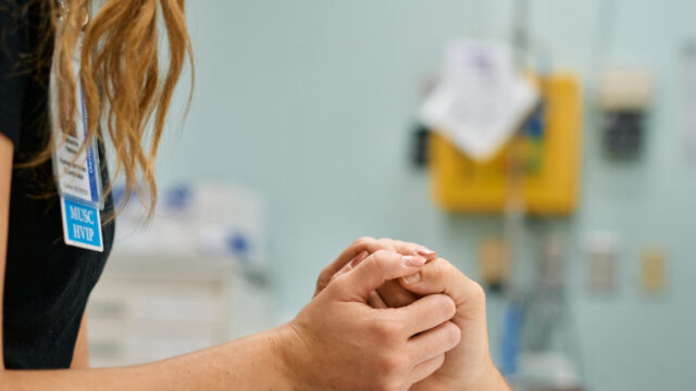 A violence prevention professional holds the hand of a patient in a medical setting, demonstrating the interaction between patients and service providers in a hospital-based violence intervention program at MUSC Health.