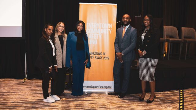 Five members of the Everytown Community Safety Fund team pose for a photo in front of an orange poster that reads: 