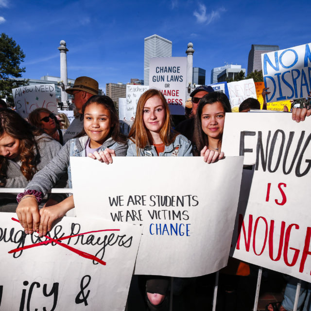 In a crowd of people, three students hold signs to stop gun violence