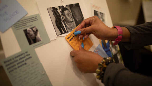 A woman pins a moment that survives post it to a board with images of those lost to gun violence