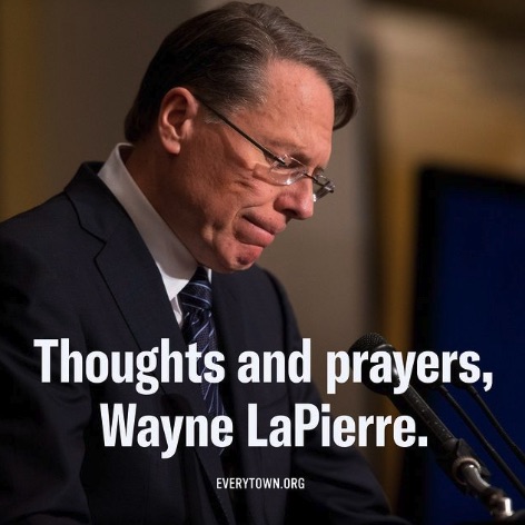 A side-profile photo of Wayne LaPierre, former NRA leader, who is standing at a podium looking down at his notes. He is a white man with grey/brown hair parted on the side. He wears frameless rectangular glasses, a white collared shirt, a navy blazer, and a navy-striped tie. The bottom of the photo reads "Thoughts and prayers, Wayne LaPierre." in white text.