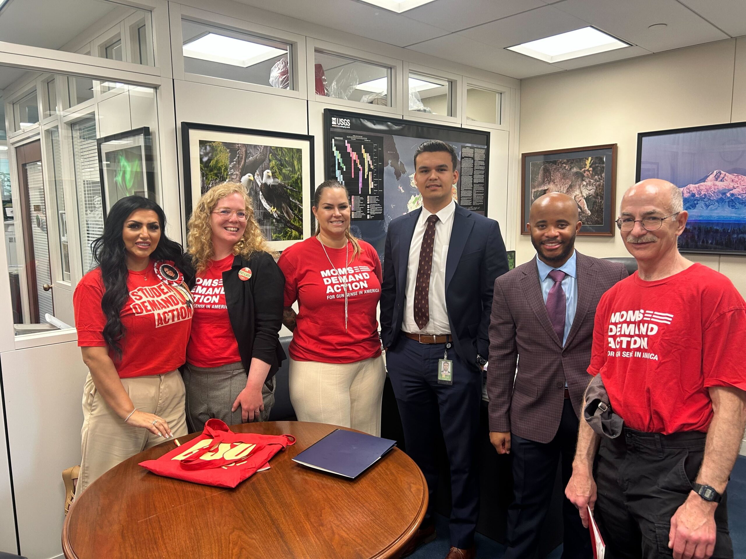 Moms Demand Action volunteers meeting with a staffer from Sen. Dan Sullivan's office. Three Moms Demand Action volunteers stand to the right of the staffer; two others stand to his left. The group is smiling and standing in a half-circle.