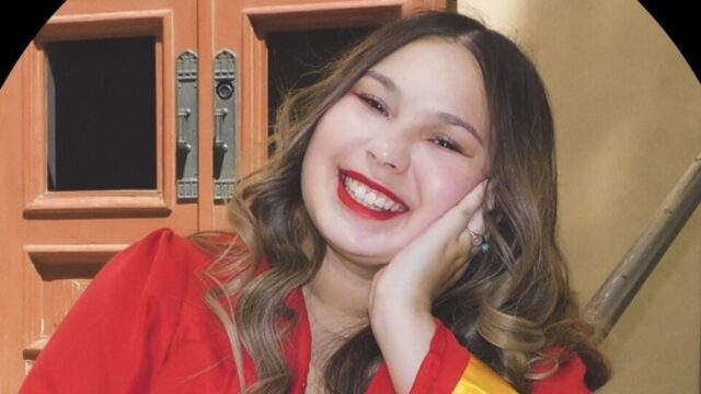 Leighanne Muñoz, a student volunteer, poses for a photo. She rests her head on her left hand and is wearing a red graduation robe with a gold ribbon that circles the sleeve about an inch from the cuff. Her long hair is curled and parted in the middle.