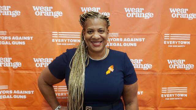 Mayor Shawyn Patterson-Howard wearing an orange ribbon in front of a Wear Orange backdrop