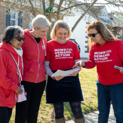 A group of four volunteers in Moms Demand Action shirts look at a piece of paper while door knocking