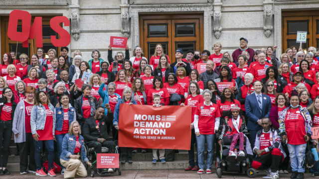 A diverse group of Moms Demand Action volunteers pose for a photo in front of the Ohio Capitol Building during an Ohio Moms Demand Action Advocacy Day. The crowd is filled with 
