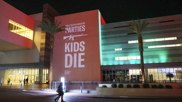 Photo of person walking by SHOT Show wall installation: While the gun industry parties, kids die