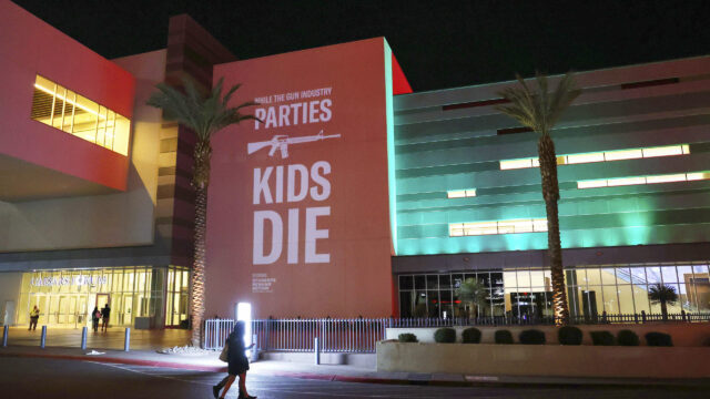 Photo of person walking by SHOT Show wall installation: While the gun industry parties, kids die