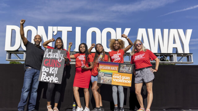 Students Demand Action volunteers raise their firsts and hold signs in front of a “Don't Look Away” sign