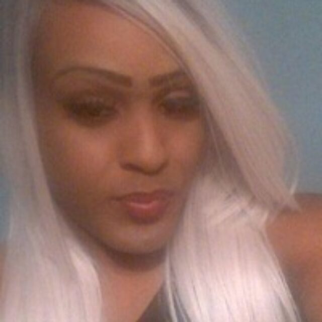 Shannon Boswell, a Black trans woman, takes a selfie. Her silver-blonde hair is long, falls below her shoulders, and is parted on the side. She wears a black sleeveless top.