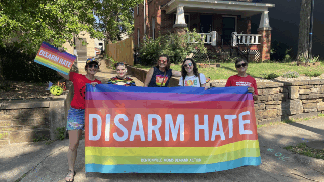 Moms Demand Action volunteers hold up a rainbow Disarm Hate banner