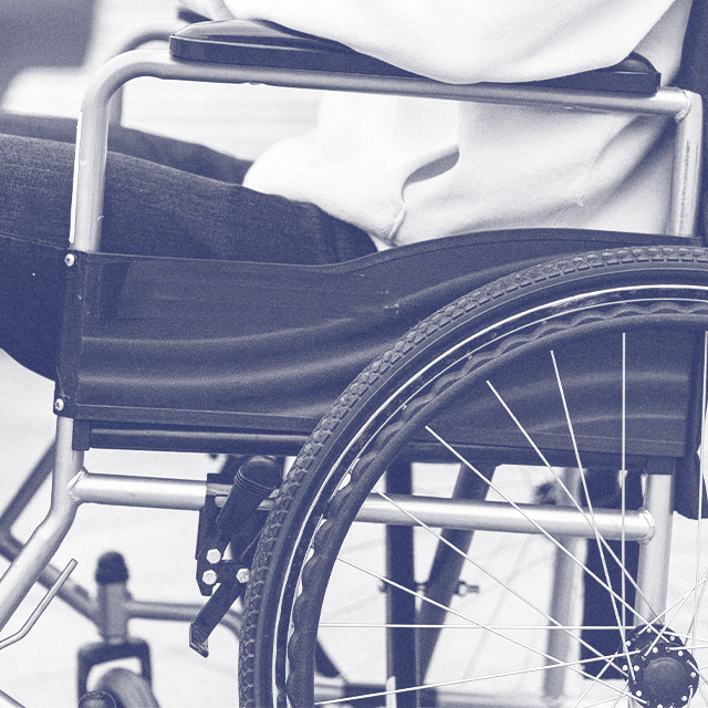 A close-up side profile of a person sitting in a wheelchair; their thighs, torso, and forearm are visible.